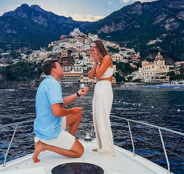 A man proposing on one knee to his partner on the bow of a private yacht charter in Positano during a luxury wedding proposal boat tour.