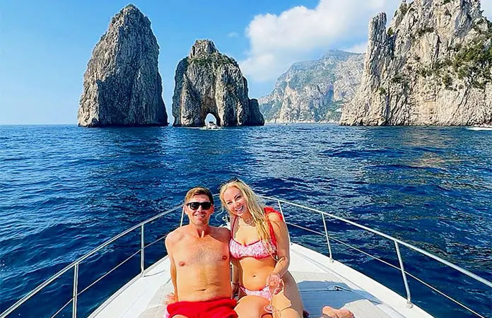 Couple relaxing on the deck of a private yacht charter in front of the Faraglioni rocks in Capri during a luxury boat excursion